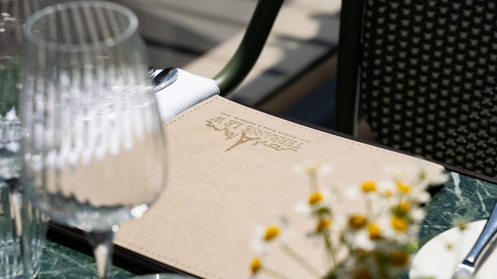 Table dressée avec menu, verres et fleurs sur la Terrasse Le W au Warwick Paris Champs-Elysées