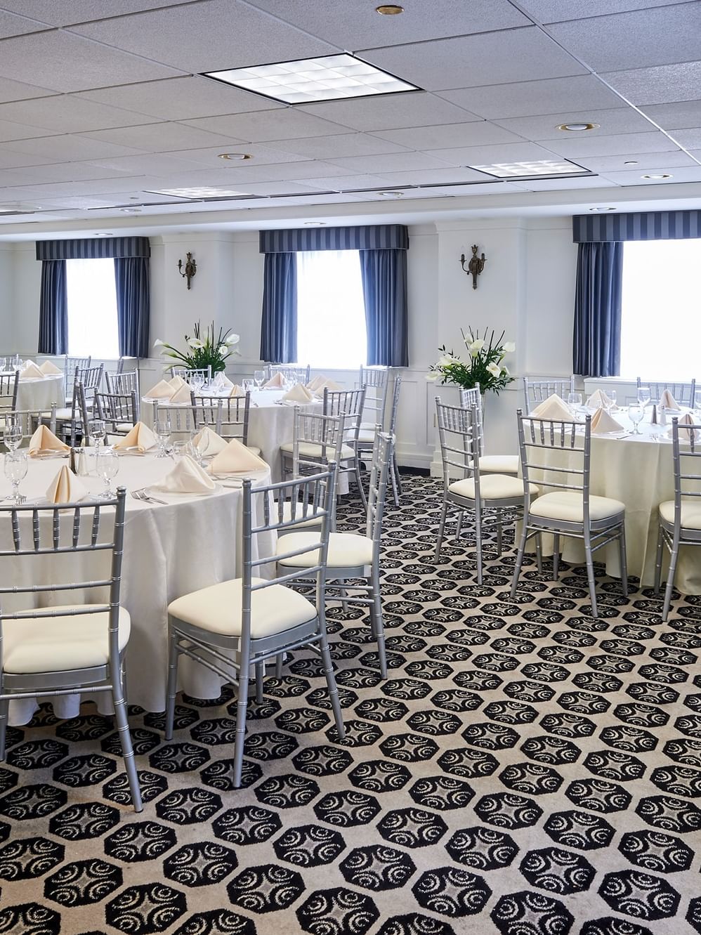Elegantly set tables with white linens and silver chairs in the Frank Lloyd Wright Room at Warwick Allerton - Chicago.