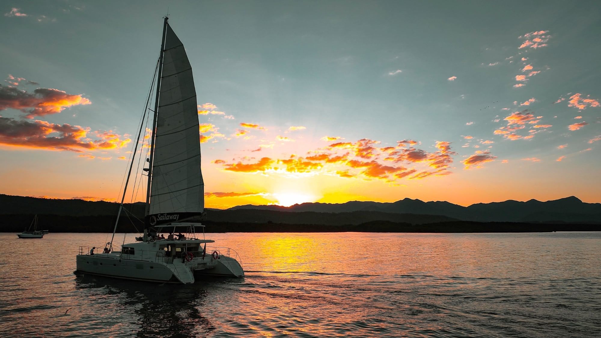 Sailboat on waters in sunset with colorful sky and mountain silhouette near Pullman Port Douglas