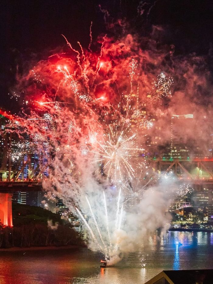 Spectacular red and white fireworks bursting over an illuminated bridge and river during New Year's Eve in Brisbane 2026.