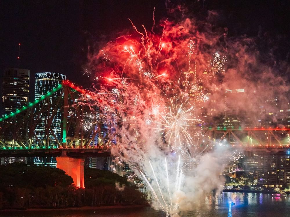 Spectacular red and white fireworks bursting over an illuminated bridge and river during New Year's Eve in Brisbane 2026.