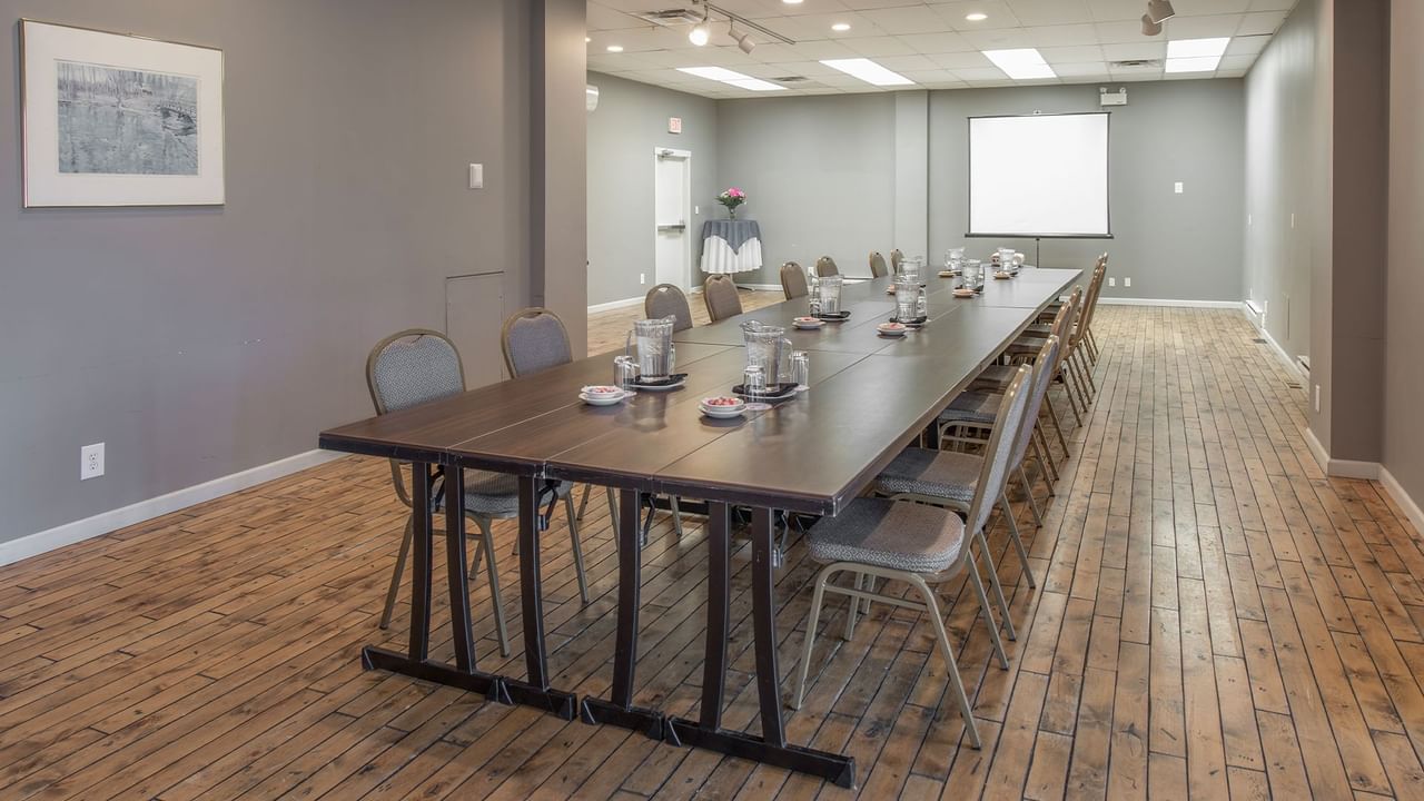 Long table with chairs in a meeting room and a white projector screen.