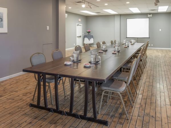 Long table with chairs in a conference room, picture frame on the wall, and a projection screen.