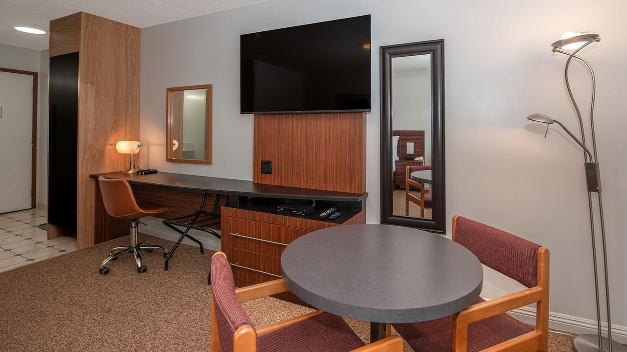 guest room with dining table, chairs, desk and wall-mounted TV at Coast Whitecourt Hotel