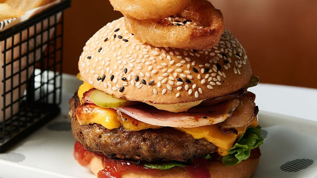 Close-up of juicy burger served with onion rings on top in Mortimer's Lounge at Pullman Albert Park