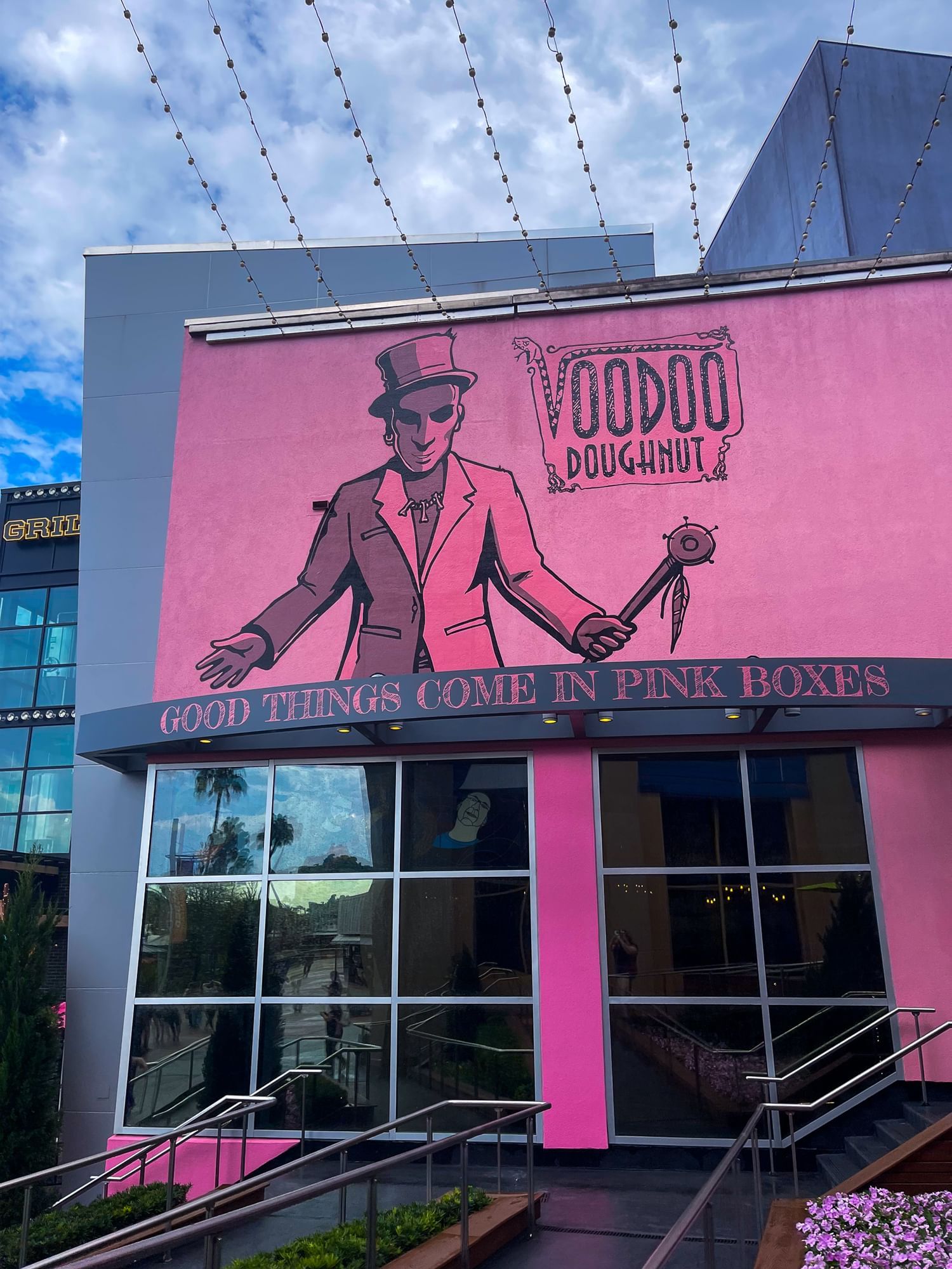 A bright pink building with a man in a mask and suit that reads "Voodoo Doughnut - Good things come in pink boxes."