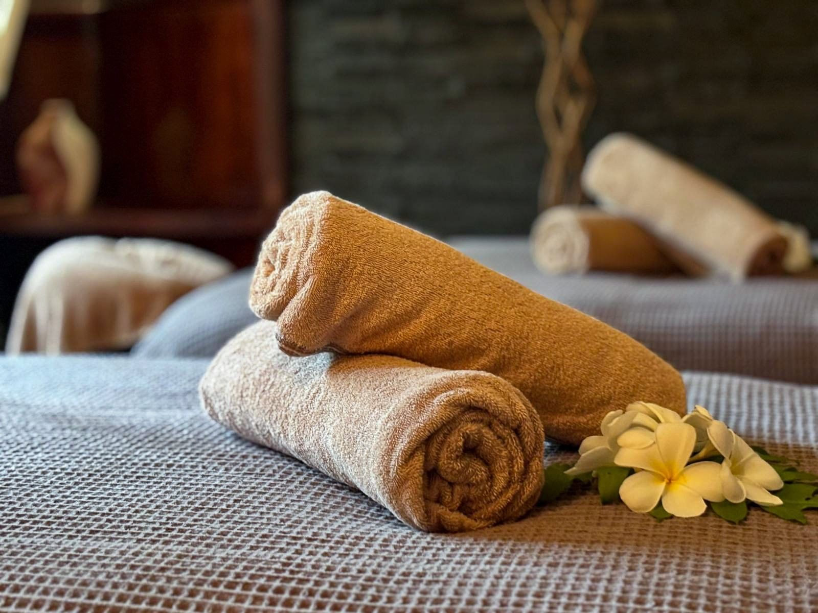 Rolled tan towels by white frangipani flowers on a grey textured bed at Warwick Fiji Resort and Spa
