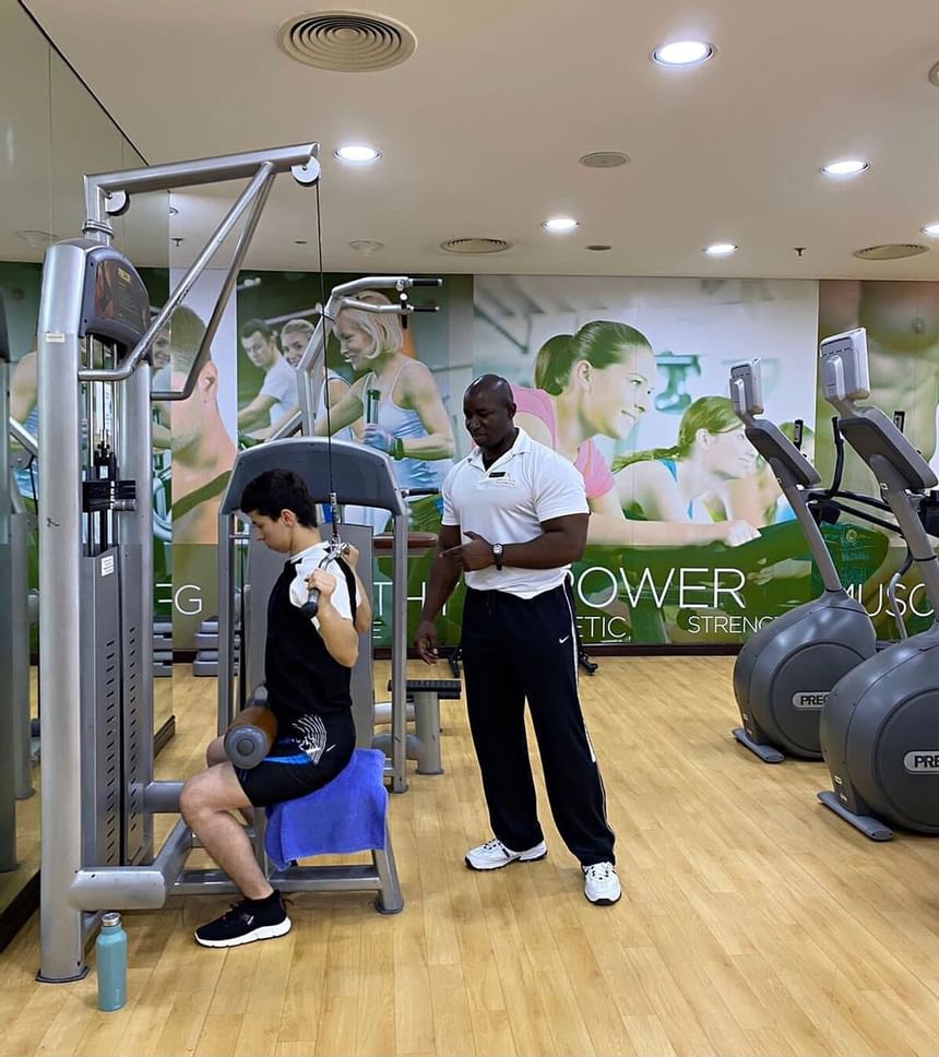 A man helped by a trainer in the gym at 2 Seasons Hotel & Apt