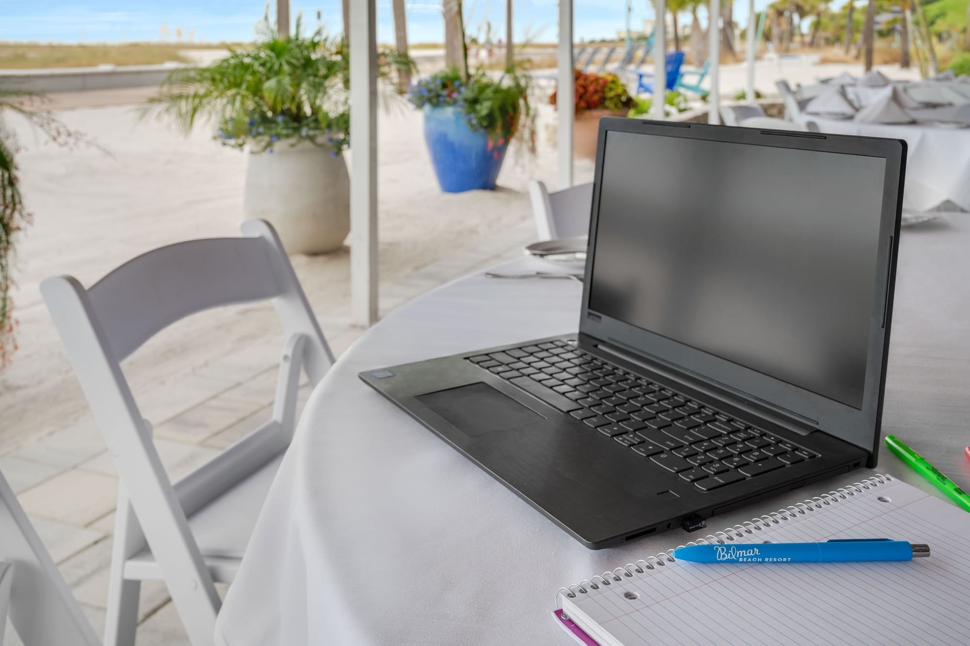 A laptop and notebook on a table with a beach background