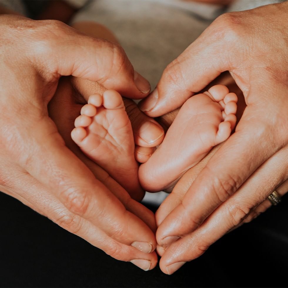 Mani formando un cuore attorno a piedini di neonato per Babymoon a Montafon.