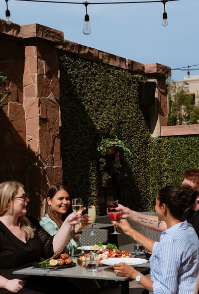 Group of happy friends raising their cocktail glasses for a toast on a sunlit outdoor dining patio at Gattara