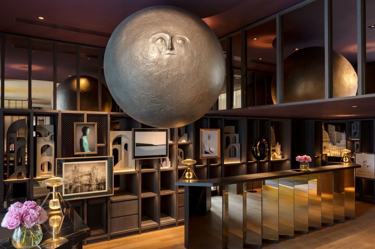 Luxurious interior of lobby at The Londoner with a large spherical sculpture, mirrored reception desk, and floral accents