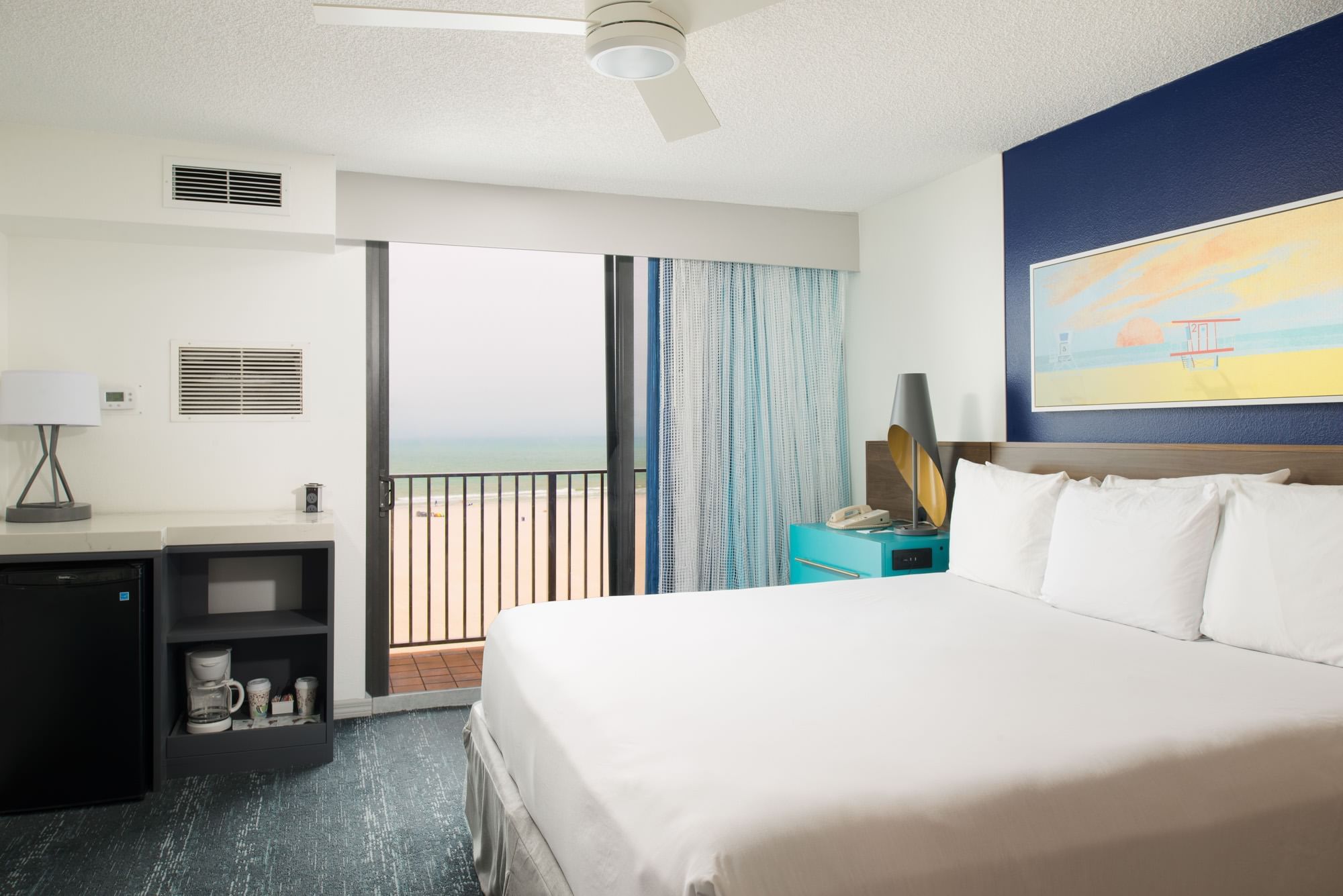 A hotel room with a bed, nightstand, balcony, and ocean view.
