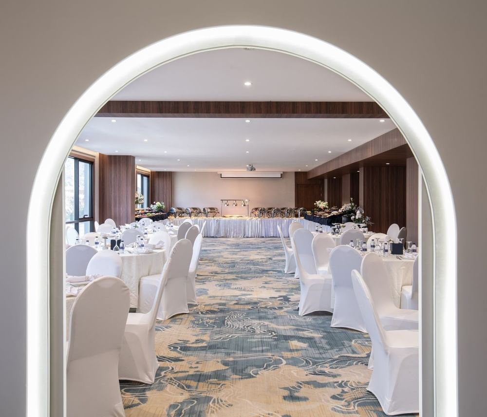Dining tables with white chairs by an arched doorway under soft spotlights at Warwick Al Taif Hotel