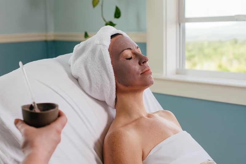 Woman relaxing with hair wrapped in a towel receiving facial mask treatment at Tower Spa in Mountain View Grand Resort & Spa