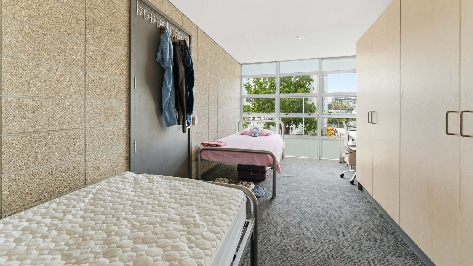 Two beds, clothes, and balcony with trees in a student living room.