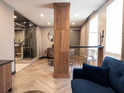 Modern hotel room with wooden pillar, glass shower, and blue couch at Carriage House Hotel & Conference Centre
