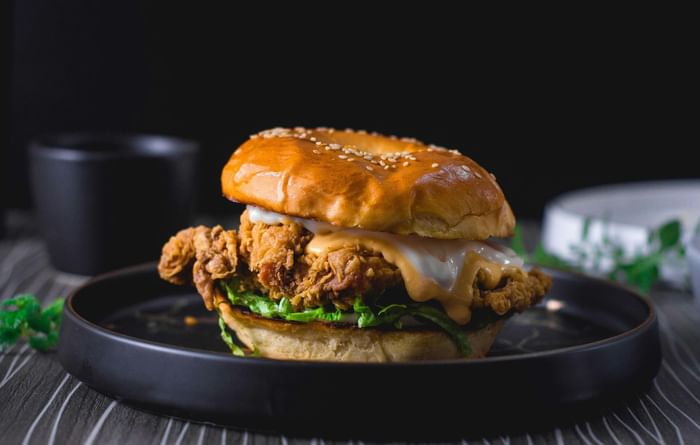 Crispy chicken bagel sandwich with melting cheese on a dark plate served at Anaheim Portofino Inn & Suites
