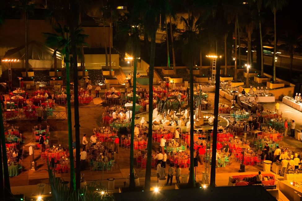Colorful evening event with setup tables lit by lights and surrounded by palm trees at Marquis Los Cabos Resort