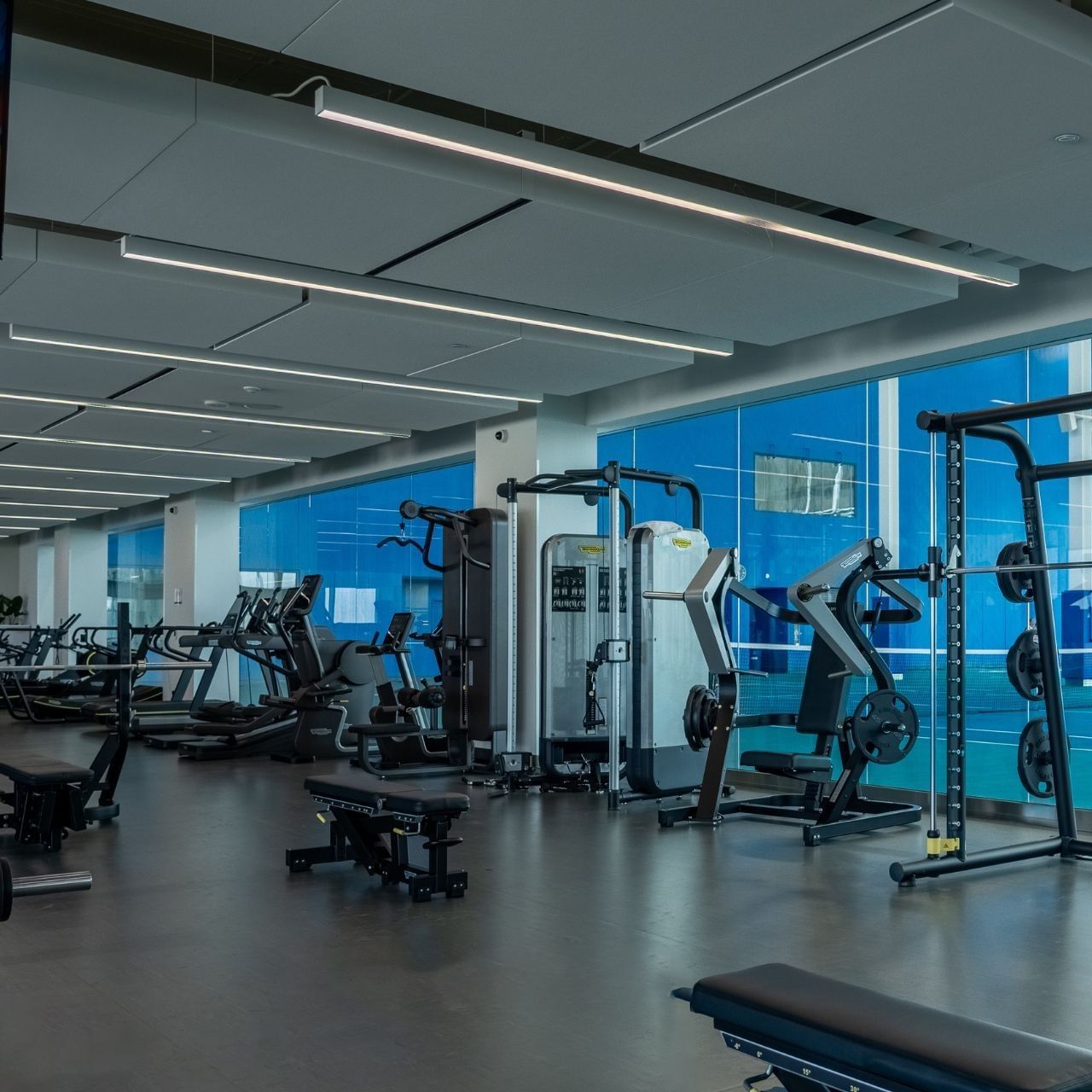 Modern fitness center with weight training equipment and floor-to-ceiling windows overlooking tennis court at 10XTO
