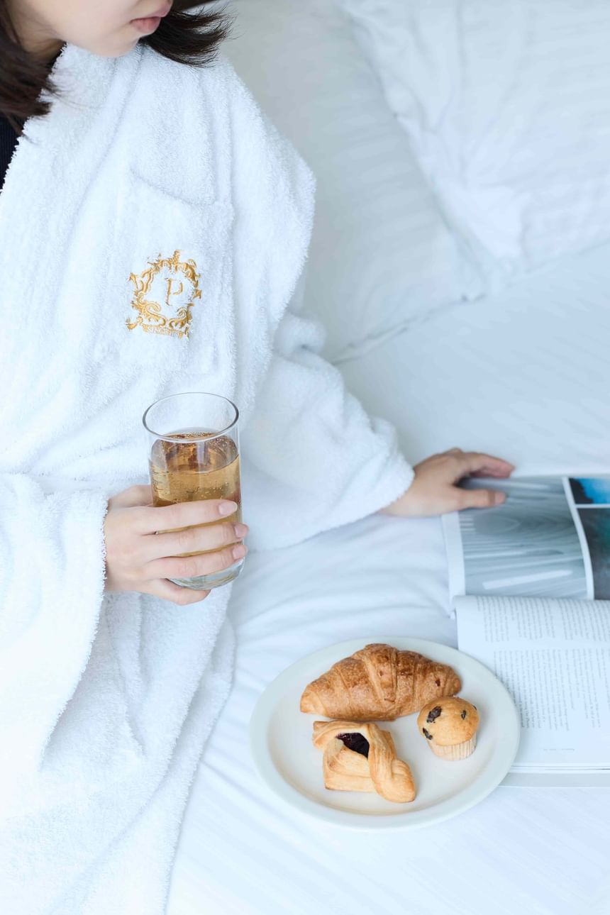 住客穿著白色浴袍，在香港百樂酒店客房床上享用點心與飲品