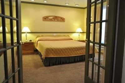 Deluxe One Bedroom Suite provide a welcoming view with a queen bed and a yellow quilted comforter at Americana Village Suites