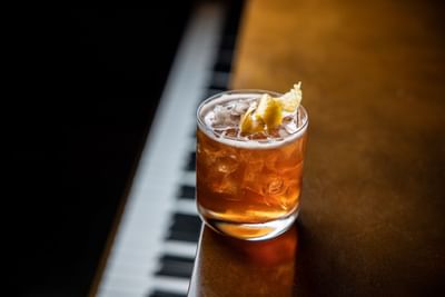 A classic cocktail with a lemon twist rests on a piano at the bar of the Royal on the Park Hotel
