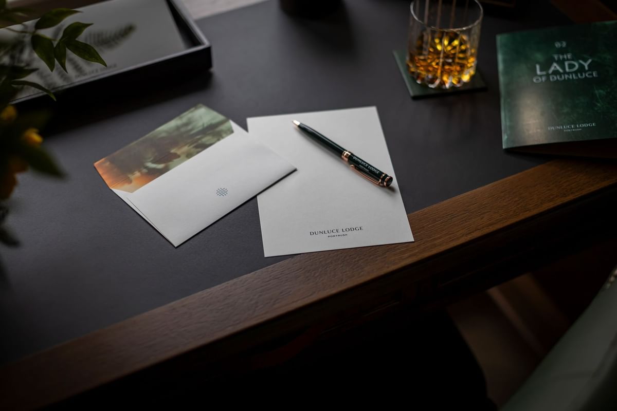 The elegant guest stationery, a pen, and a glass of whiskey on a wooden desk at Dunluce Lodge