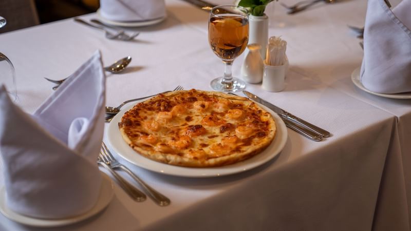 A shrimp pizza and wine on a table at Al Firdous in Madinah at Saja by Warwick Madinah.