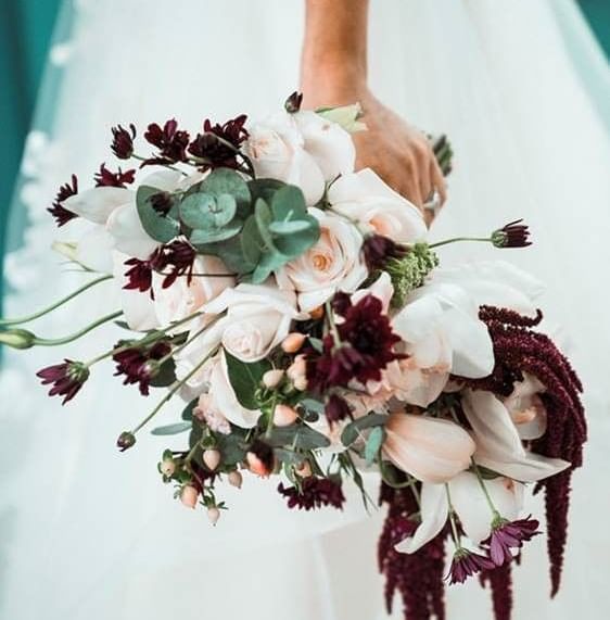 Novia sosteniendo un ramo de flores rosa claro y burdeos con hojas de eucalipto verde en Casa Santo Domingo