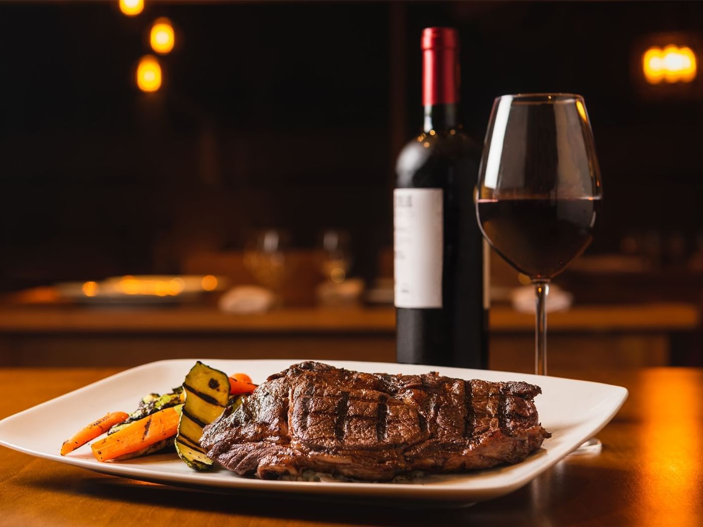 Perfectly grilled steak with vegetables and a bottle of red wine at a restaurant in Fiesta Americana