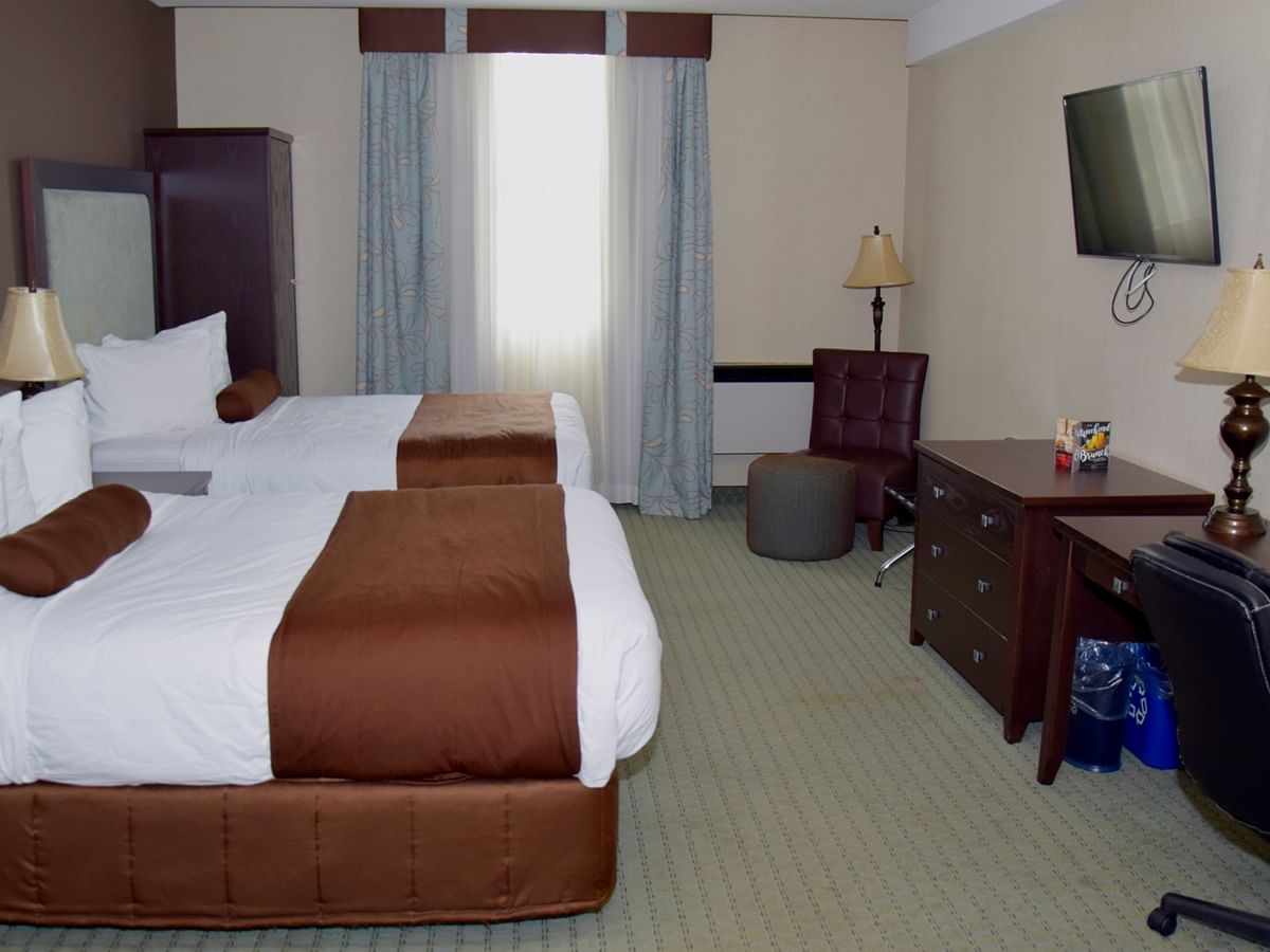 Two beds, a desk, a chair, and a window with curtains in a hotel room.