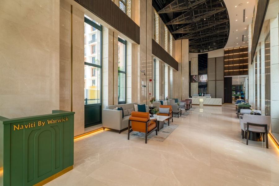 Spacious hotel lobby with high ceiling and leather armchairs near bright windows beside desk at Naviti by Warwick Jeddah