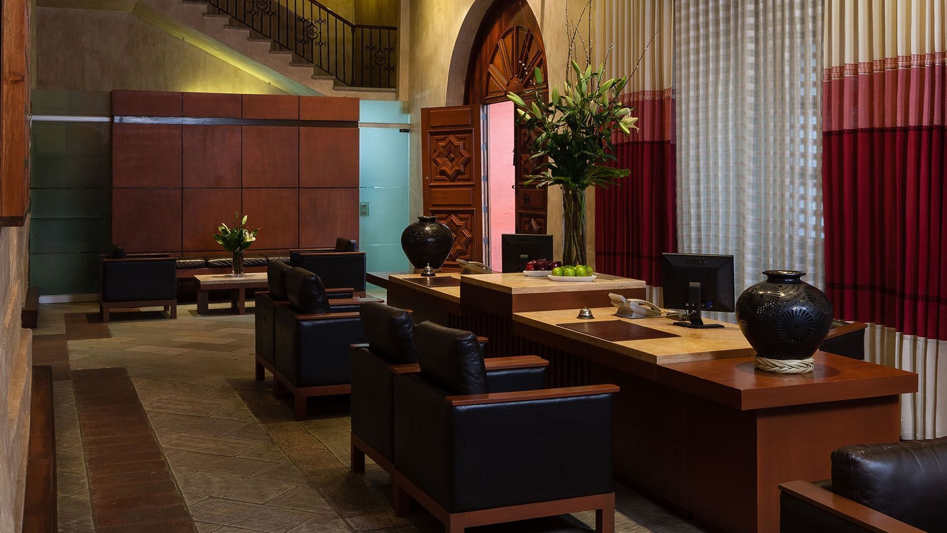 Elegant lobby with dark leather chairs, a wooden desk, and vibrant flowers at Quinta Real Oaxaca