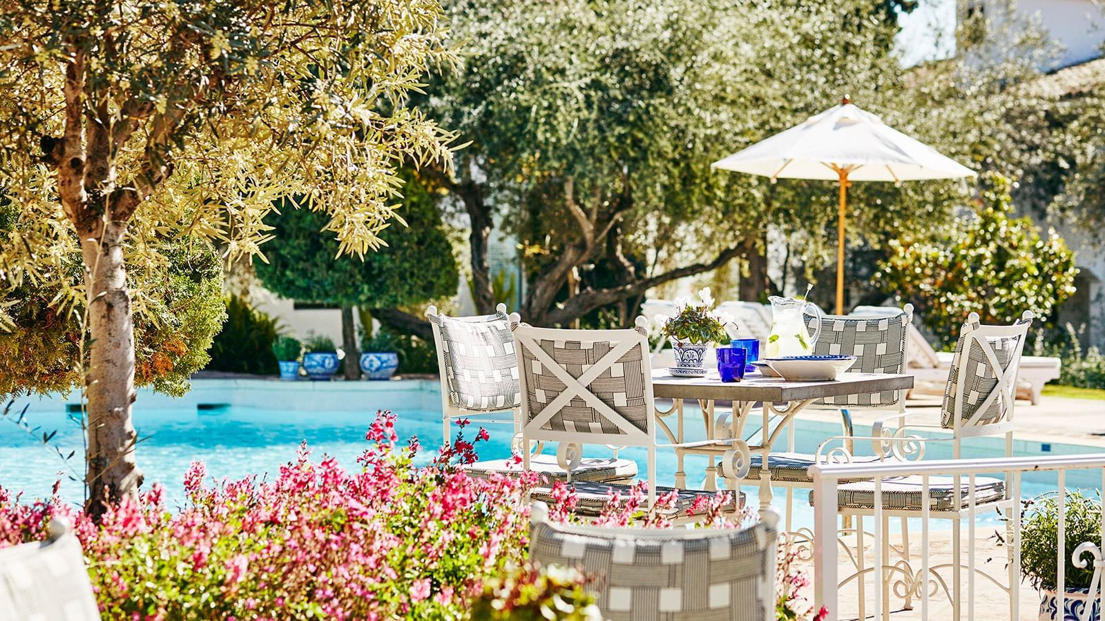 Dining set with crisscross pattern chairs placed by the sparkling pool, under an umbrella at the Marbella Club