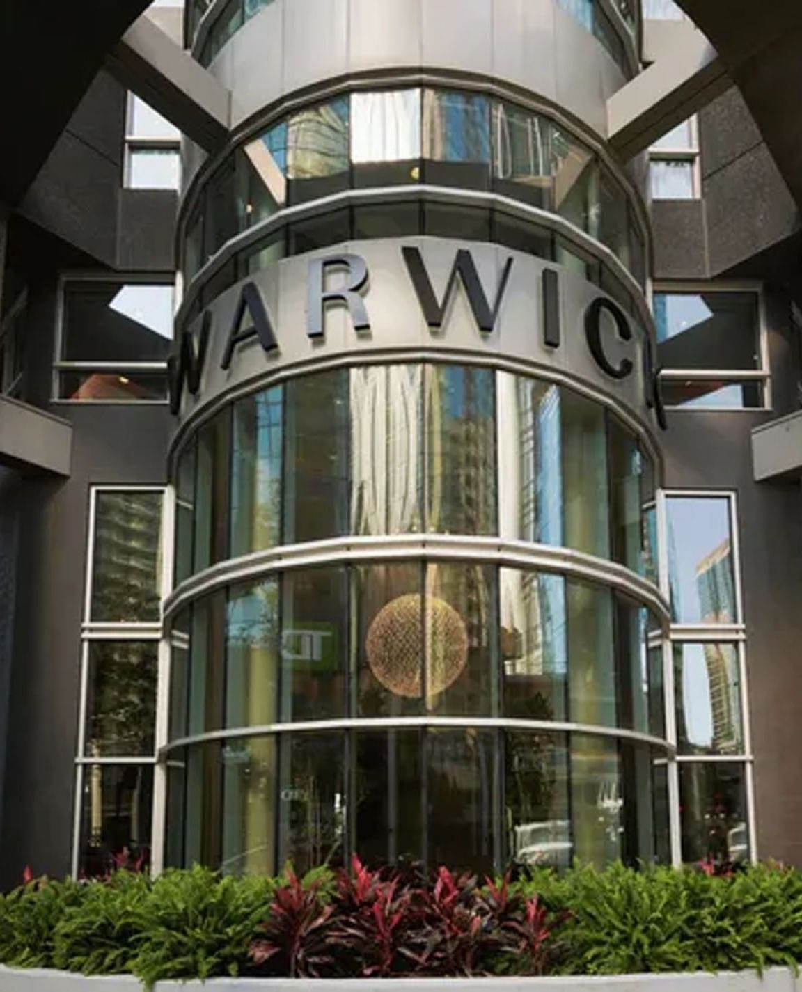Glass curved entrance with silver Warwick signage and greenery at Warwick Le Crystal Montreal