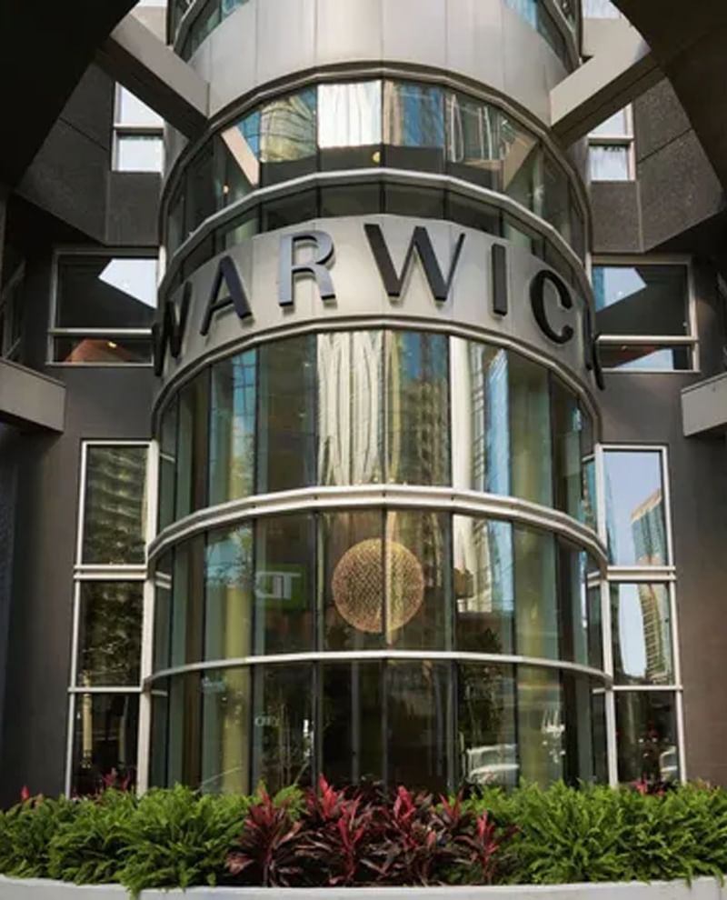 Glass curved entrance with silver Warwick signage and greenery at Warwick Le Crystal Montreal