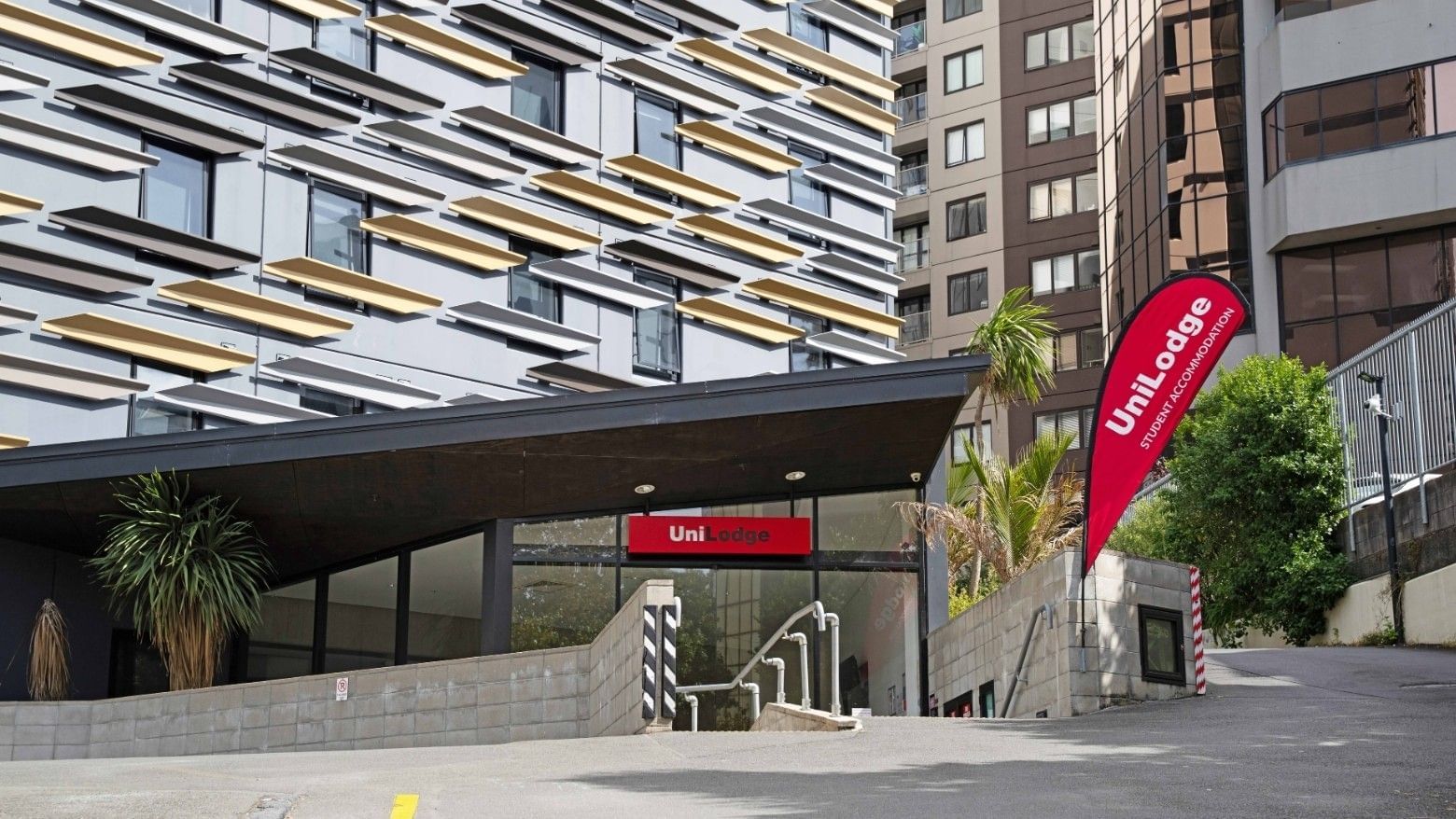 Modern UniLodge Auckland City exterior with entrance and red sign in urban setting.
