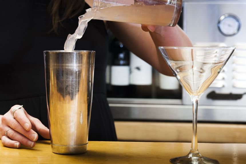 bartender pouring drink into mixer next to martini glass
