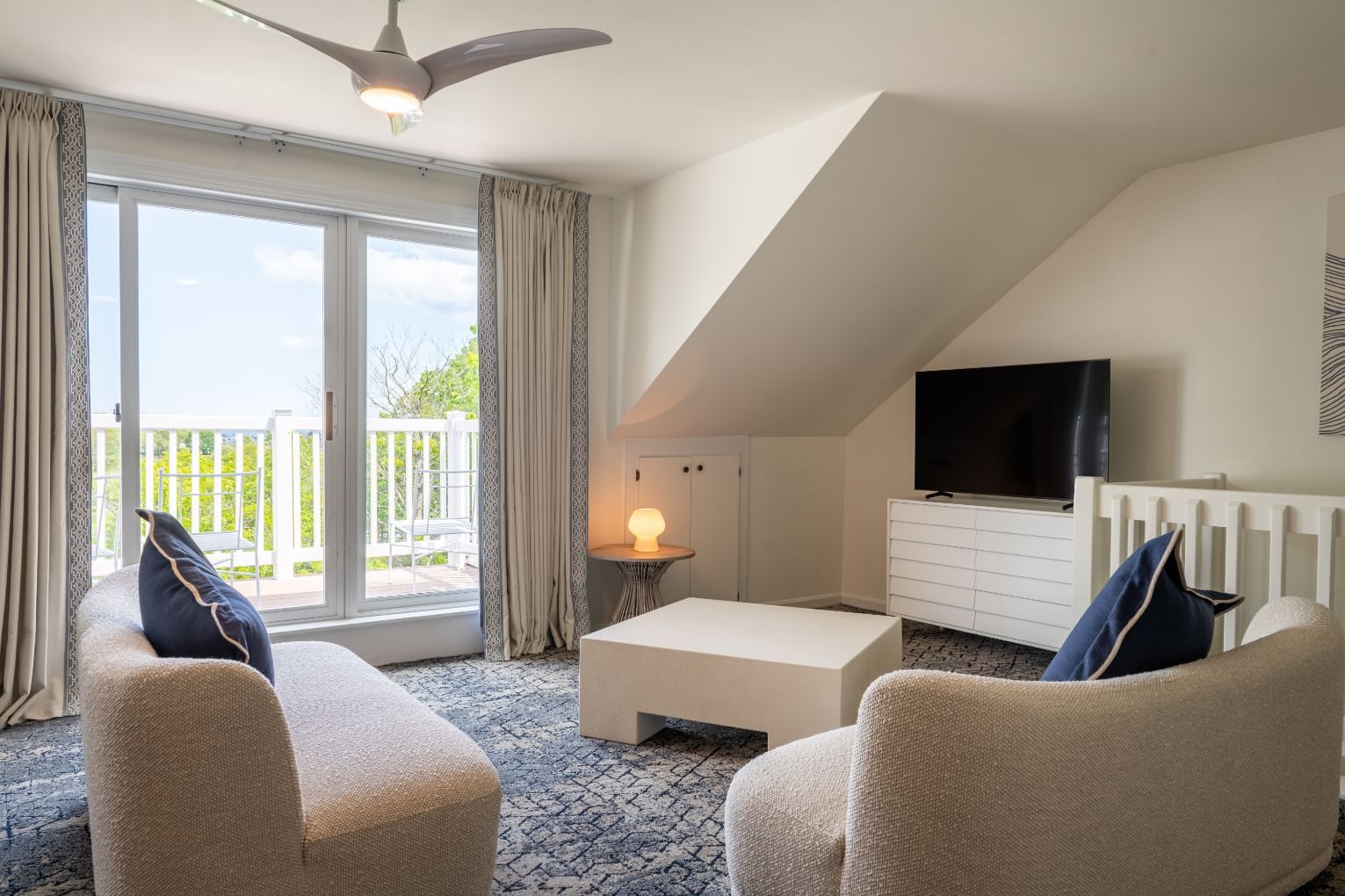 A wide view of a suite with a sofa, armchair, coffee table, TV, and balcony