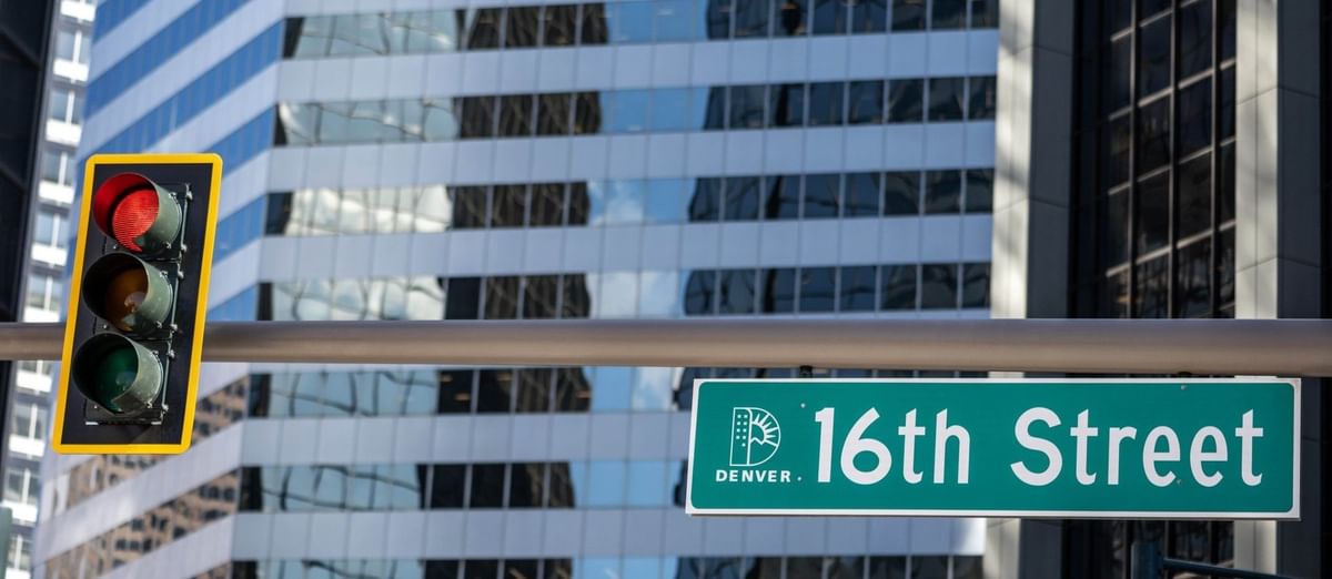Green 16th Street sign by a traffic light under a glass skyscraper at Warwick Denver