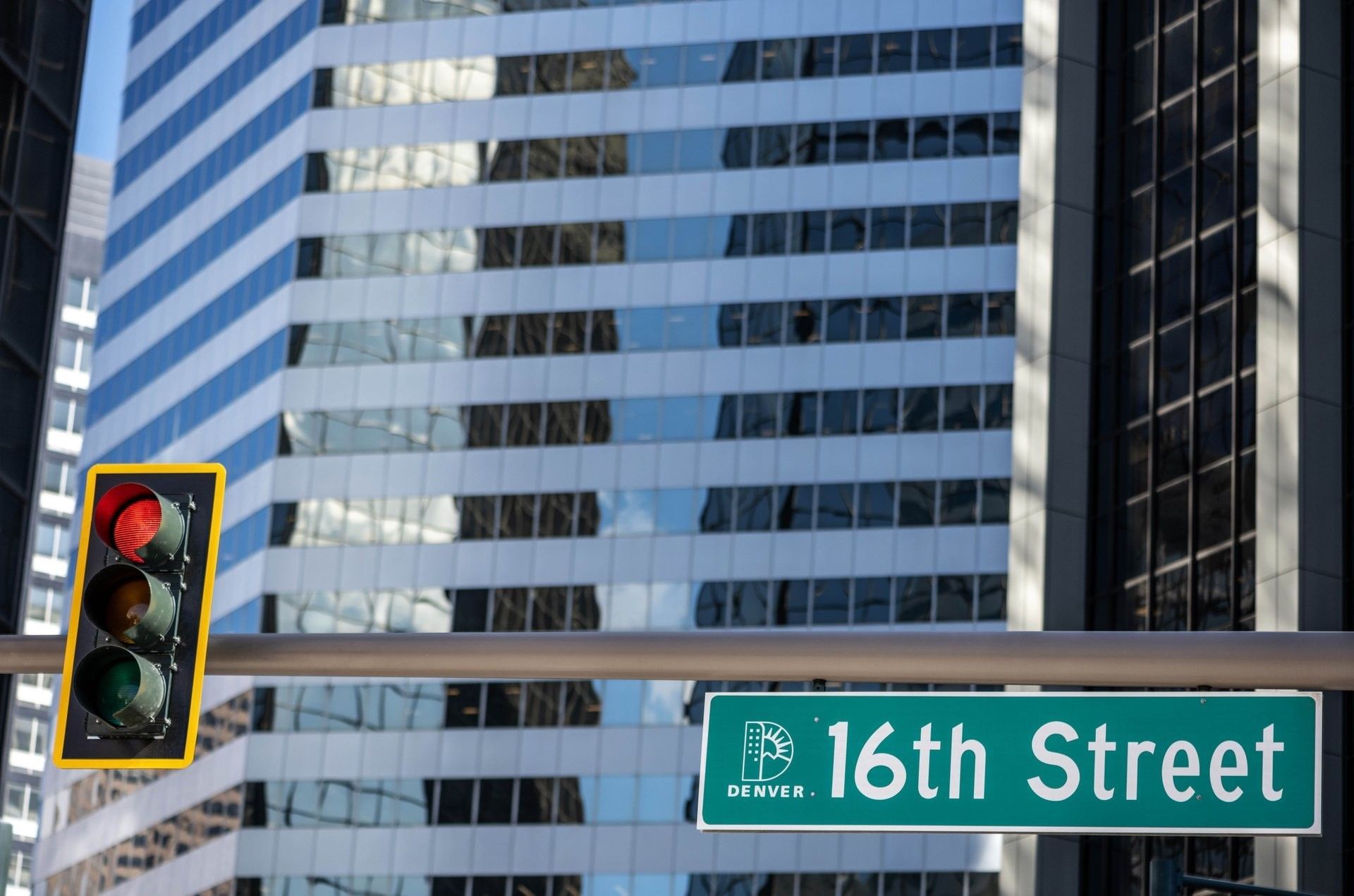 Green 16th Street sign by a traffic light under a glass skyscraper at Warwick Denver