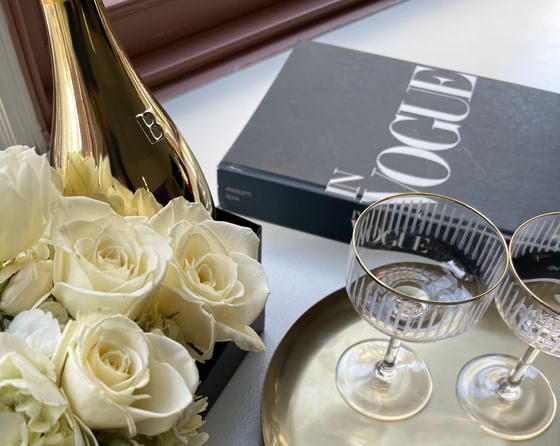 A gold champagne bottle beside a bouquet of white roses and two coupe glasses at ReStays Ottawa