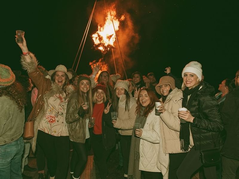 Group of people celebrating at Cabin Fever Fest with bonfire in the background