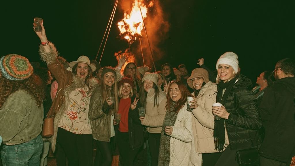 Group of people celebrating at Cabin Fever Fest with bonfire in the background