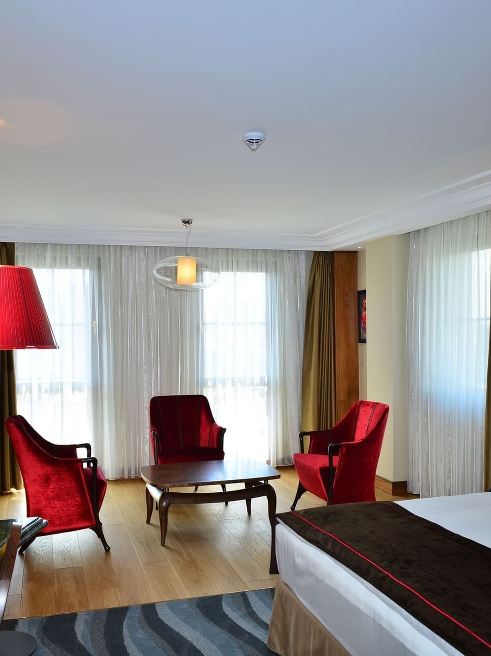 Junior Suite features Red velvet chairs by a wooden table surrounding a bright window at Warwick Ankara