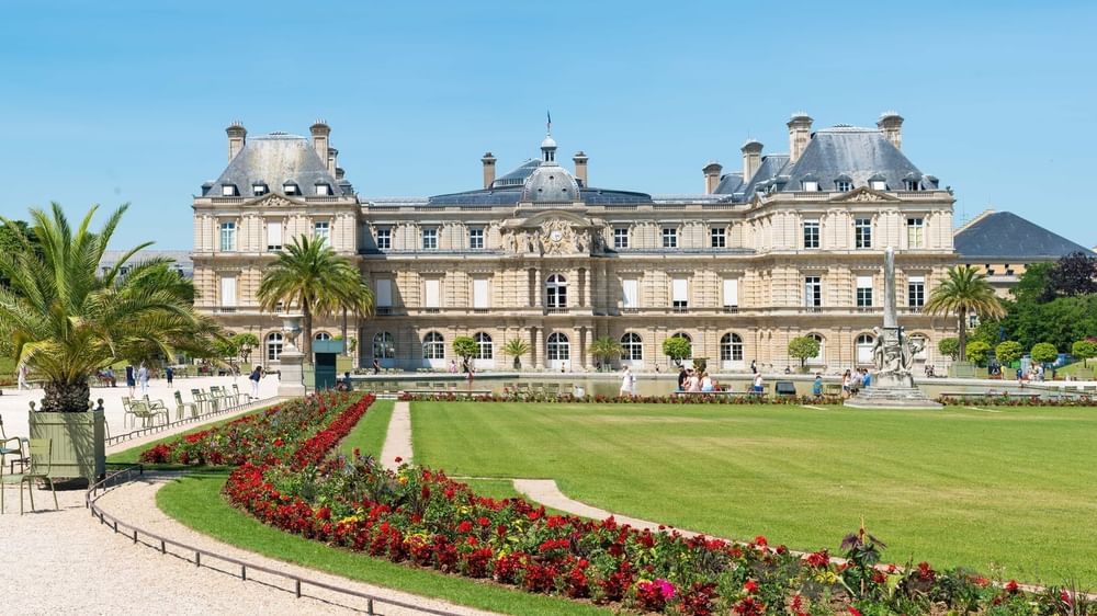 Grand palace by a wide green lawn under a clear blue sky in a garden at Warwick Paris Champs Elysées