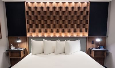 Modern room with a bed and four pillows under a wooden headboard at Carriage House Hotel & Conference Centre