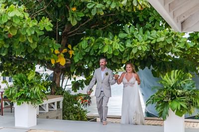 Bride and groom walking outdoors under tropical trees at 
Beach wedding venues in Roatan Barefoot Cay Resort & Marina