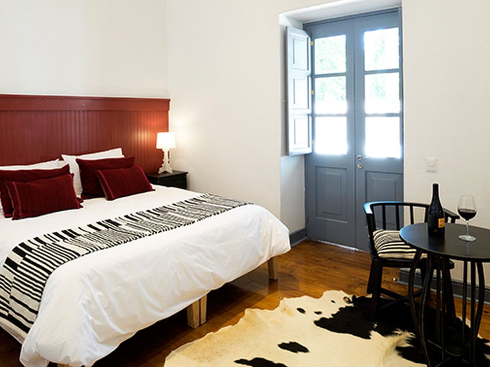 Cama grande junto a mesa sob cabeceira sobre tapete de couro na Deluxe Italian Room do NOI Blend Colchagua